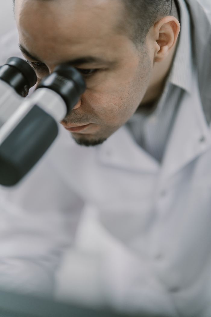 Close-up of a scientist in a white lab coat examining samples through a microscope in a research laboratory.